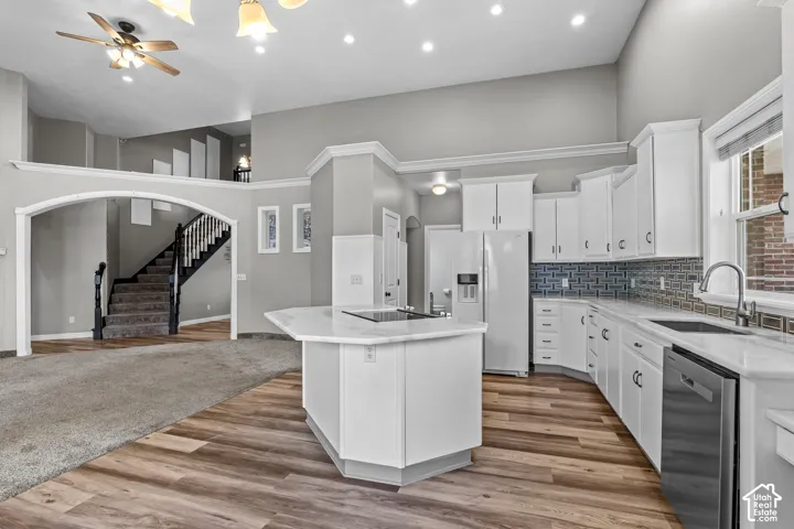 Spacious kitchen featuring white cabinetry, light-toned countertops, stainless steel appliances, a center island with a cooktop, and wood-finish flooring