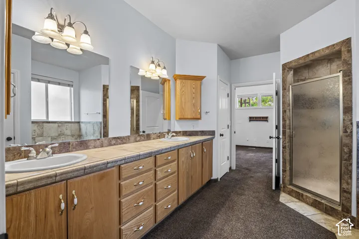 Spacious bathroom featuring a dual vanity with light wood cabinetry, tile countertops, and two integrated sinks