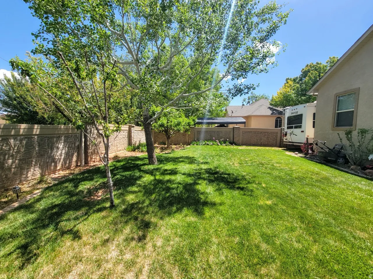 Expansive backyard featuring a lush lawn, mature trees, and a textured privacy fence