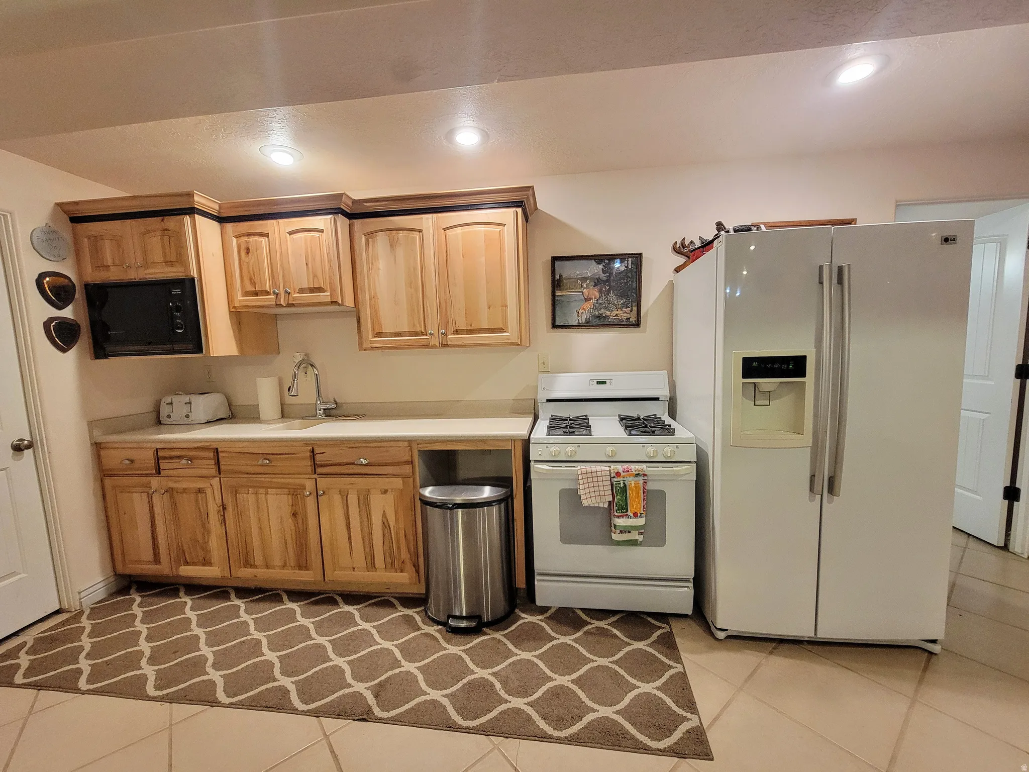 Kitchen featuring light wood cabinetry with dark trim, a stainless steel sink, and a white refrigerator with an ice and water dispenser