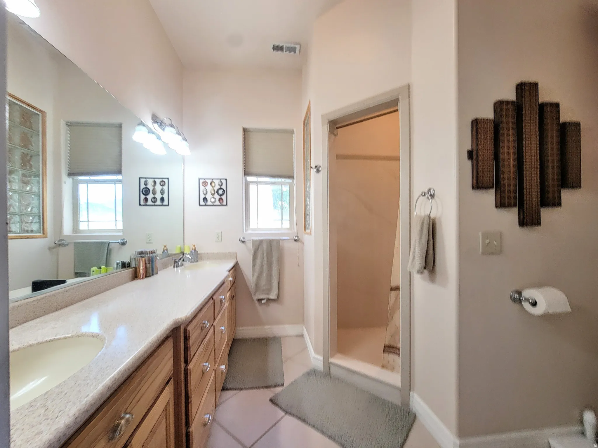 Bathroom featuring a dual vanity with light-toned countertops, wood-finish cabinetry, and an integrated mirror
