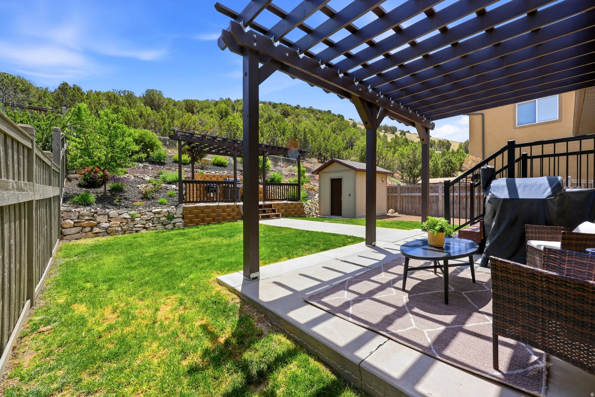 Expansive backyard featuring a concrete patio with an attached pergola, a manicured lawn, a wooden privacy fence, a detached shed, and an upper wooden deck with a second pergola