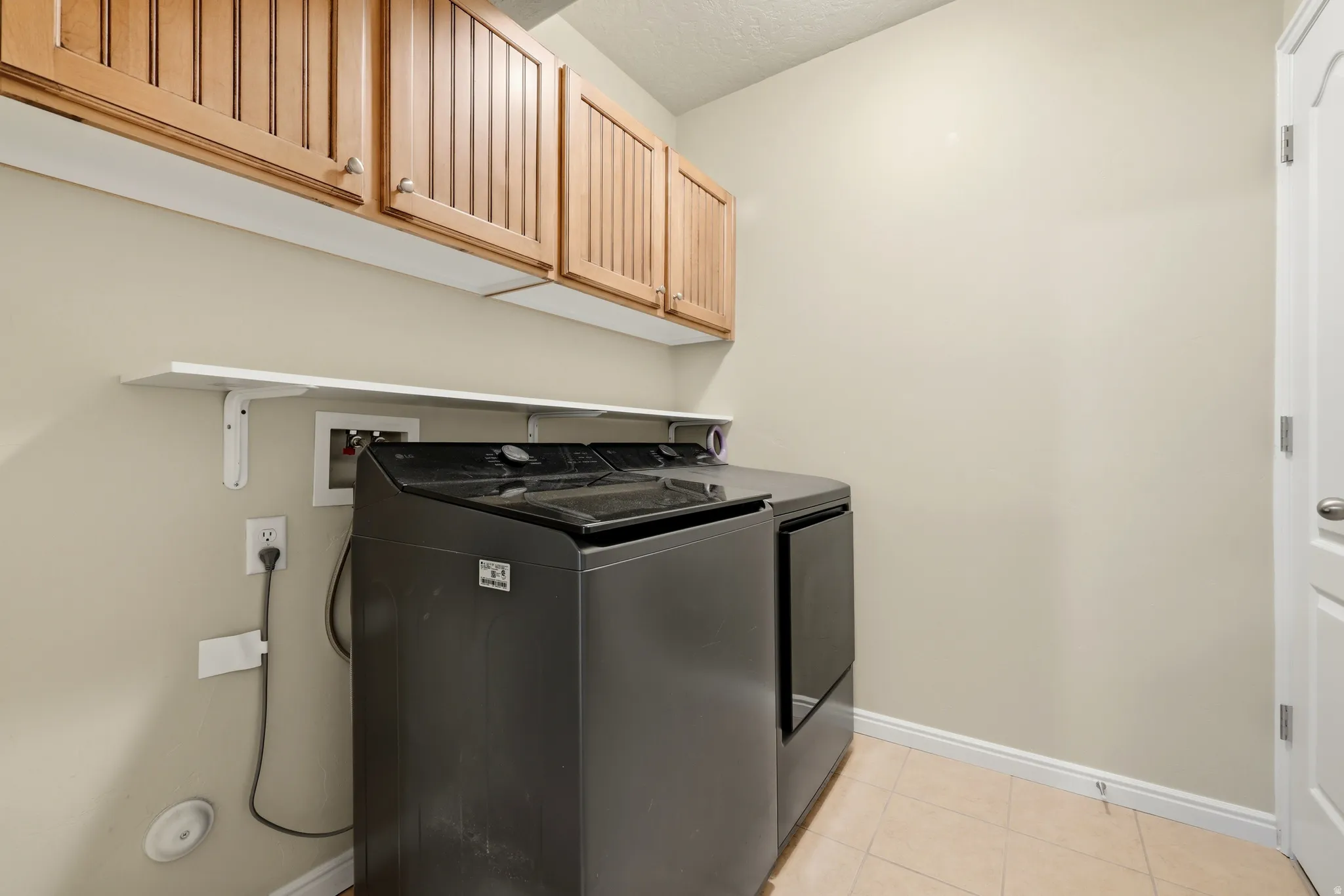 Laundry area featuring natural wood cabinetry, a white floating shelf, and neutral-toned wall paint