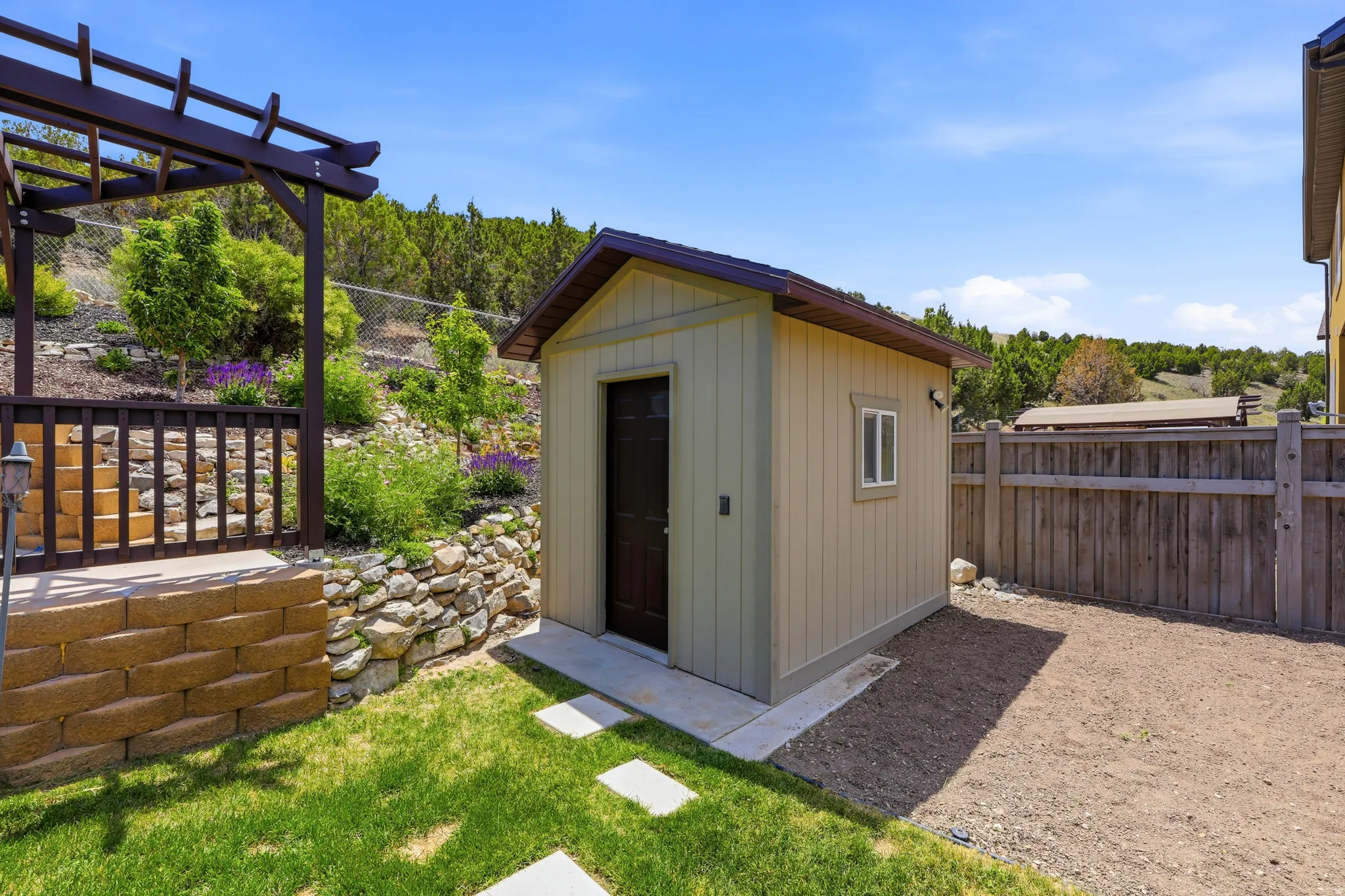 Exterior storage shed with a dark brown door and a single window, featuring an adjacent wooden privacy fence