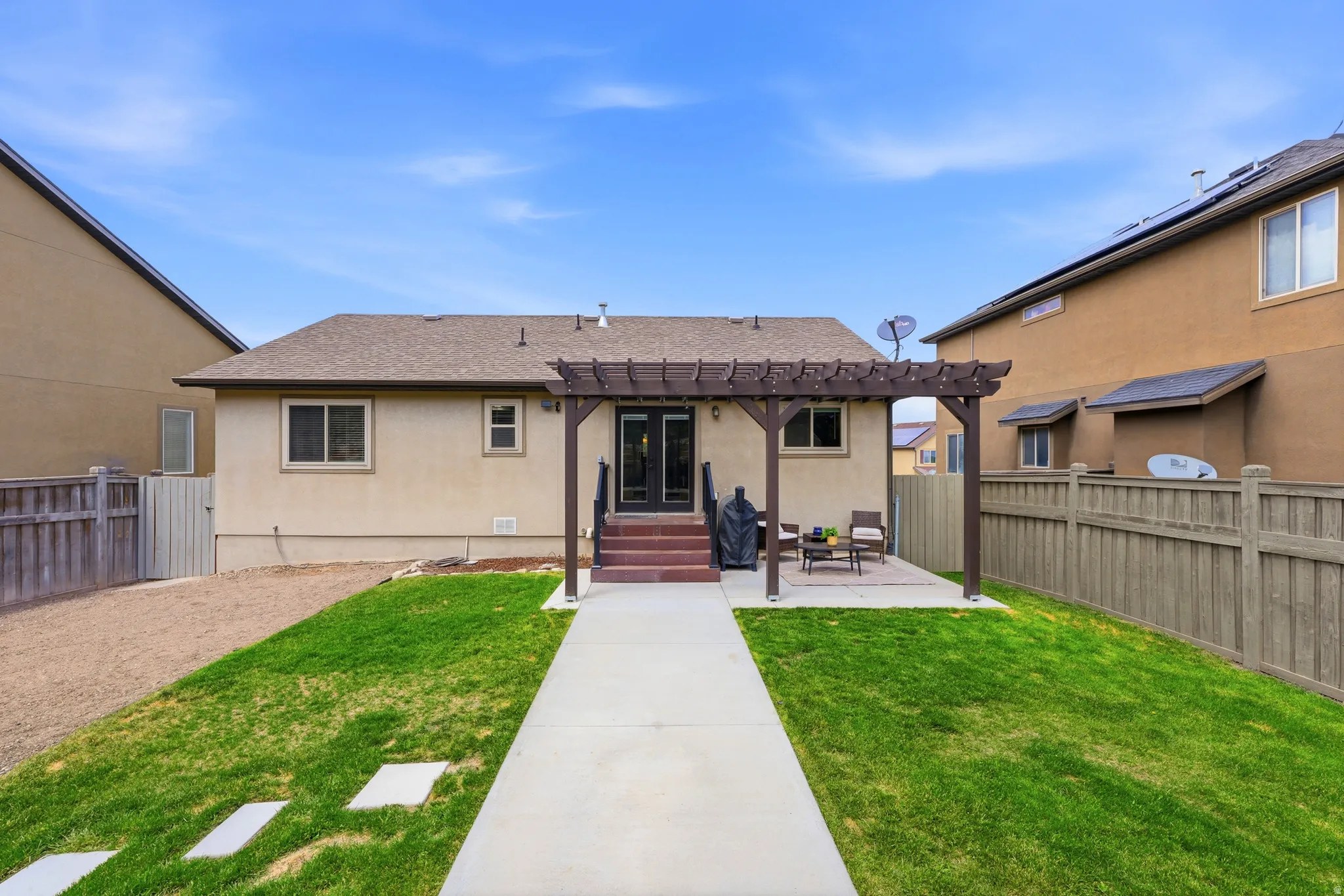 Expansive backyard featuring a concrete patio, a dark wood pergola, and a concrete pathway leading to the home's rear entrance