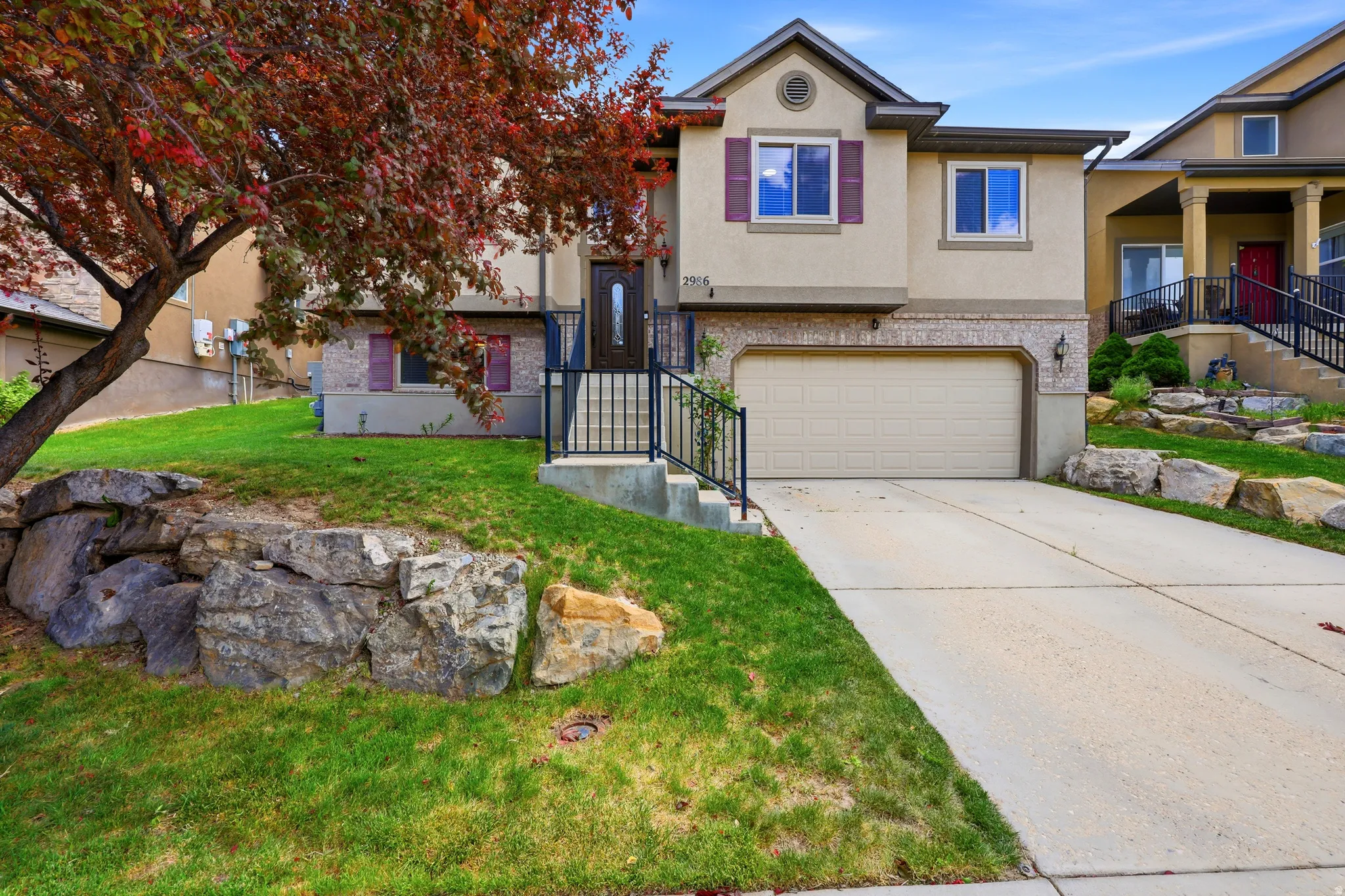 Two-story residence featuring a two-car garage, concrete driveway, and a stone retaining wall