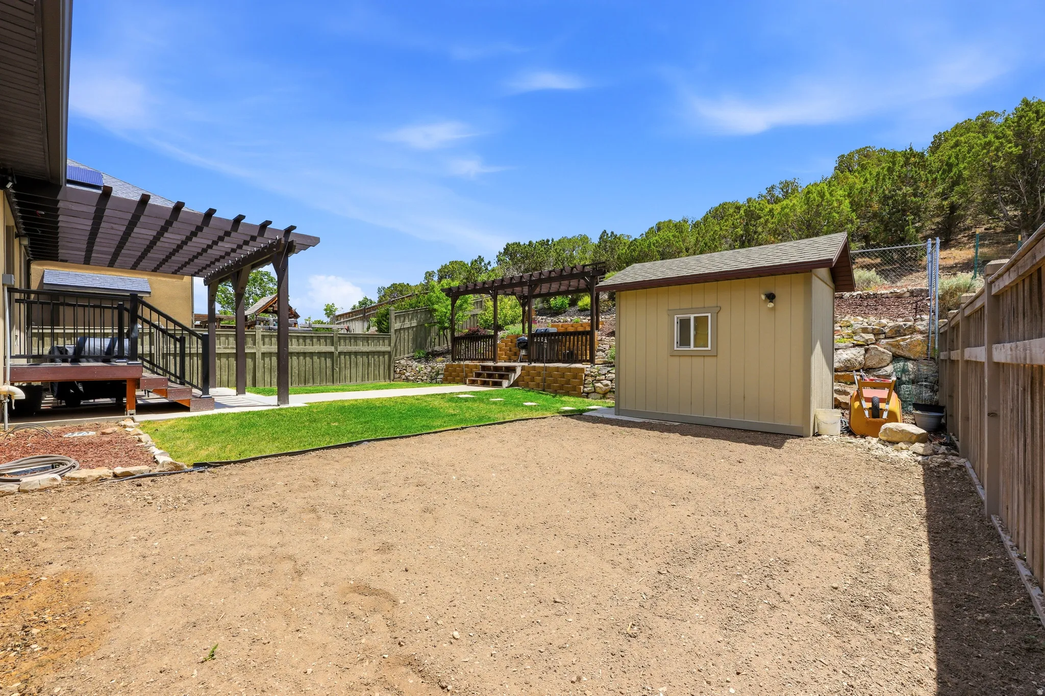 Expansive backyard featuring a wood pergola-covered deck, a dedicated storage shed, partial privacy fencing, and a terraced hillside