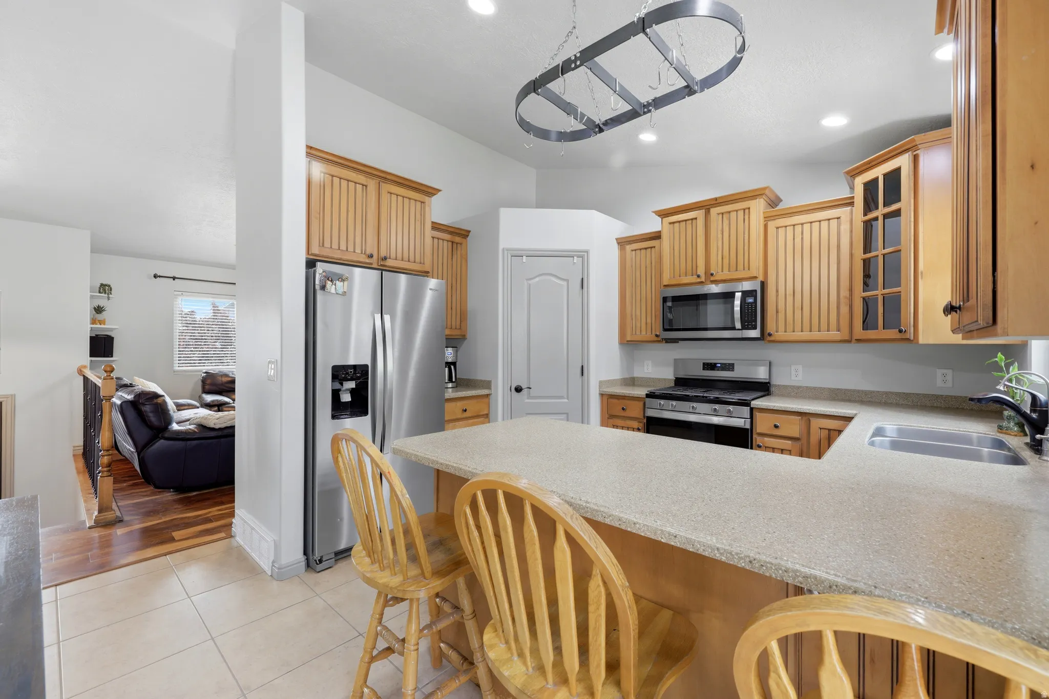 Kitchen featuring L-shaped counter seating, natural wood cabinetry, stainless steel appliances, a pot rack, and recessed lighting