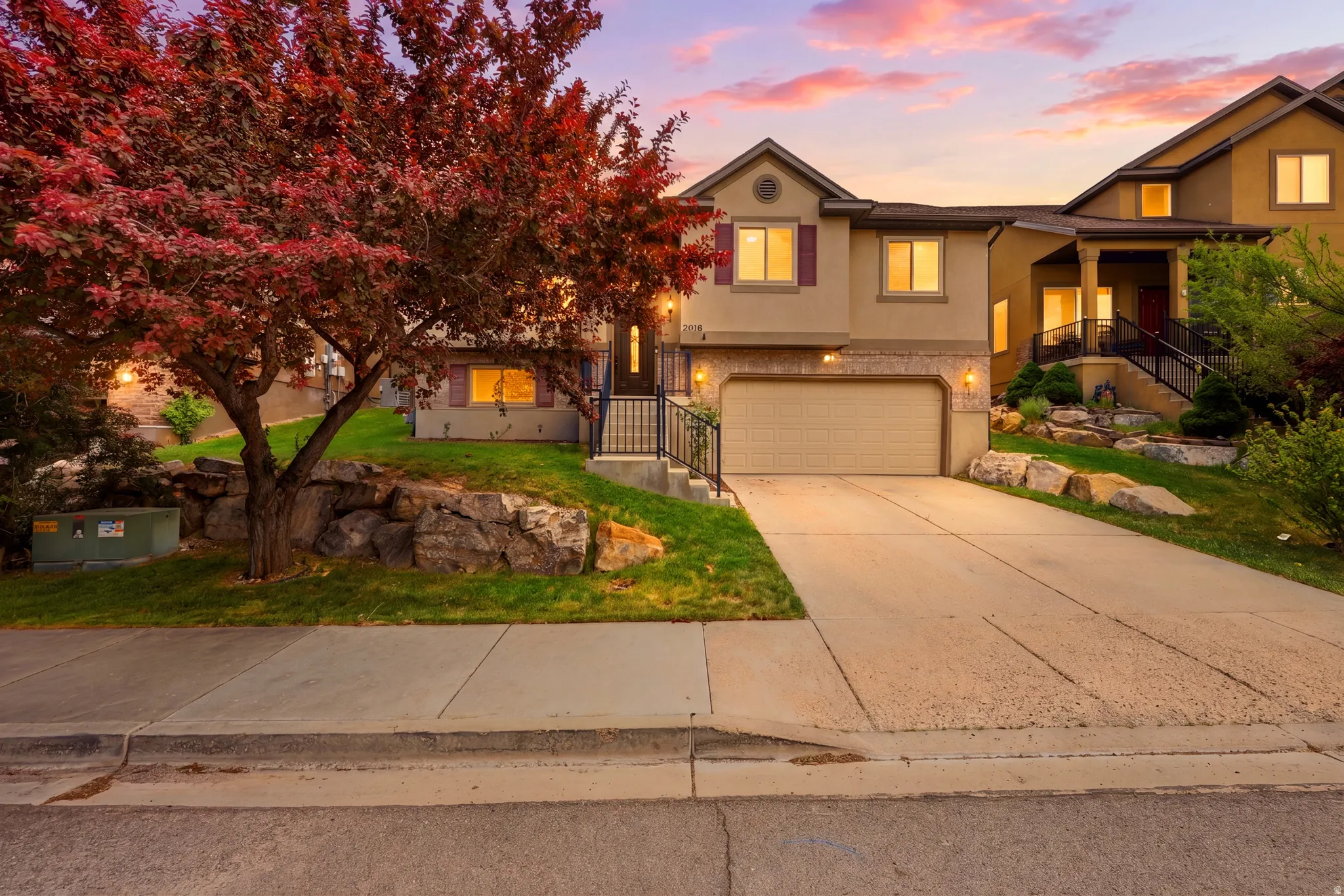 Two-story stucco exterior with a stone veneer accent, featuring a two-car garage, concrete driveway, and landscaped front yard with a mature tree