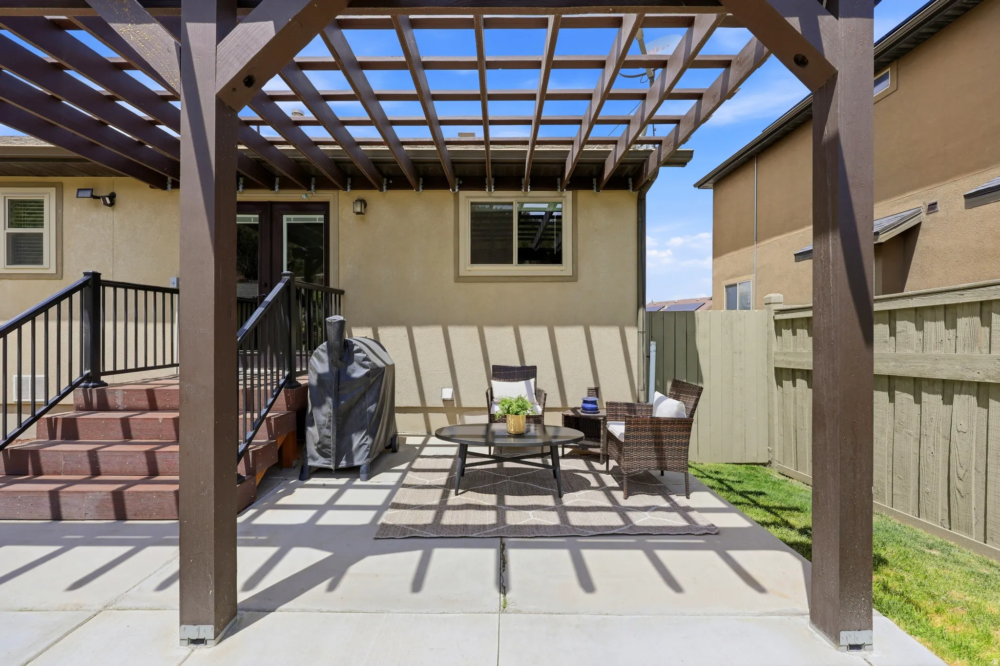Expansive concrete patio featuring a brown wood pergola, stucco exterior, freshly painted privacy fencing