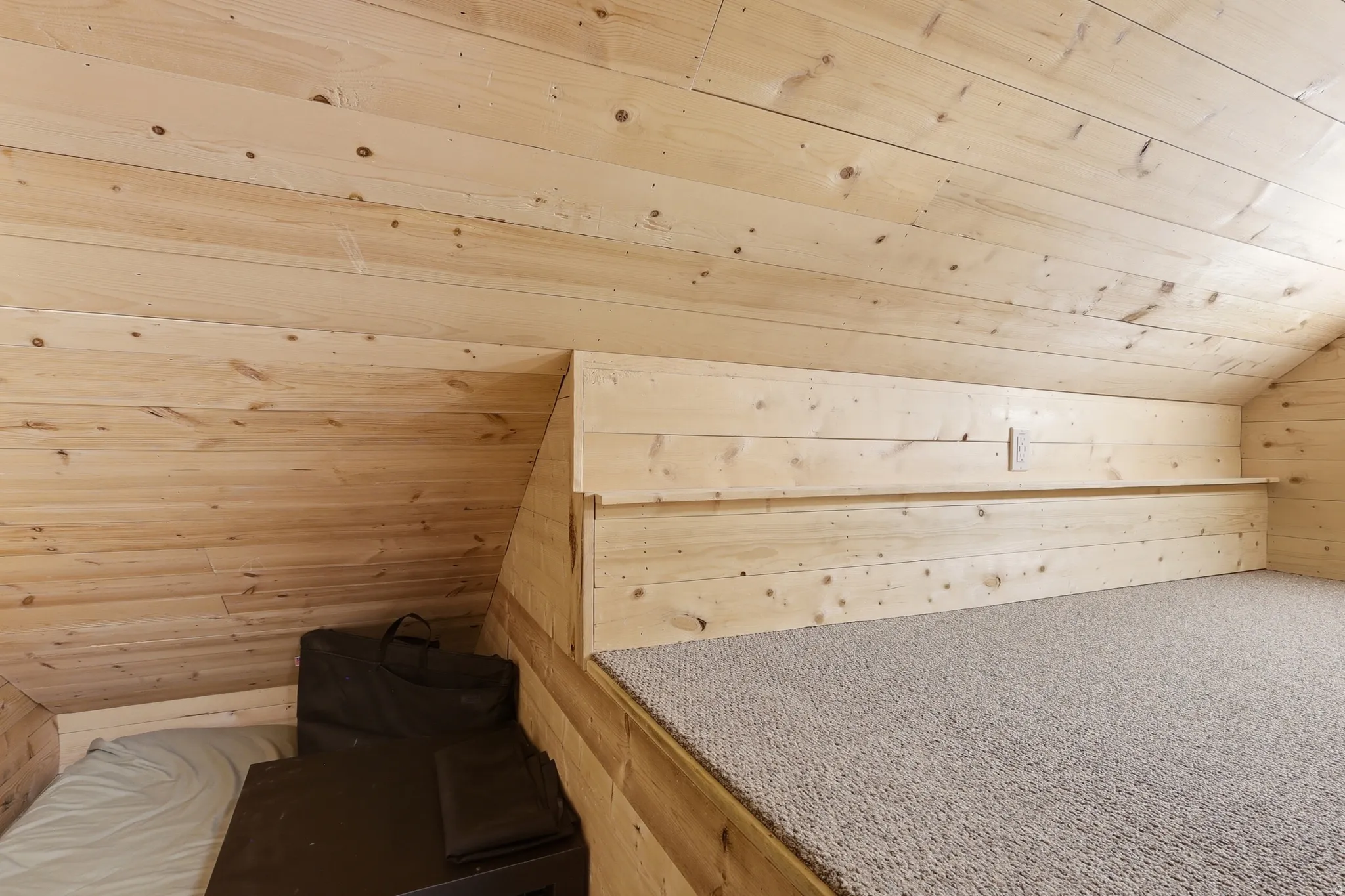 Loft sleeping area featuring light wood-finish paneling, a built-in shelf, and neutral-toned carpeting