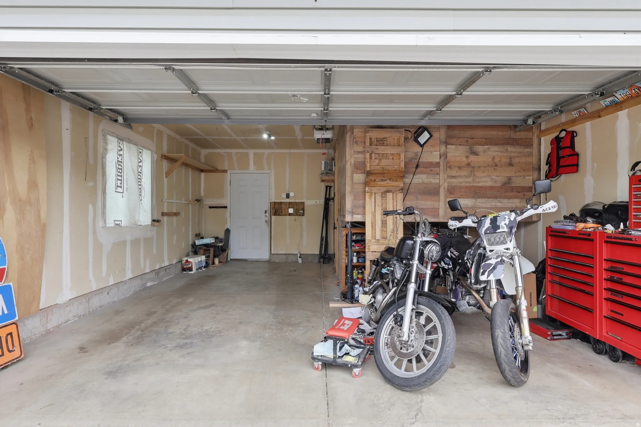 Spacious garage featuring a concrete floor, overhead lighting, and a white interior door