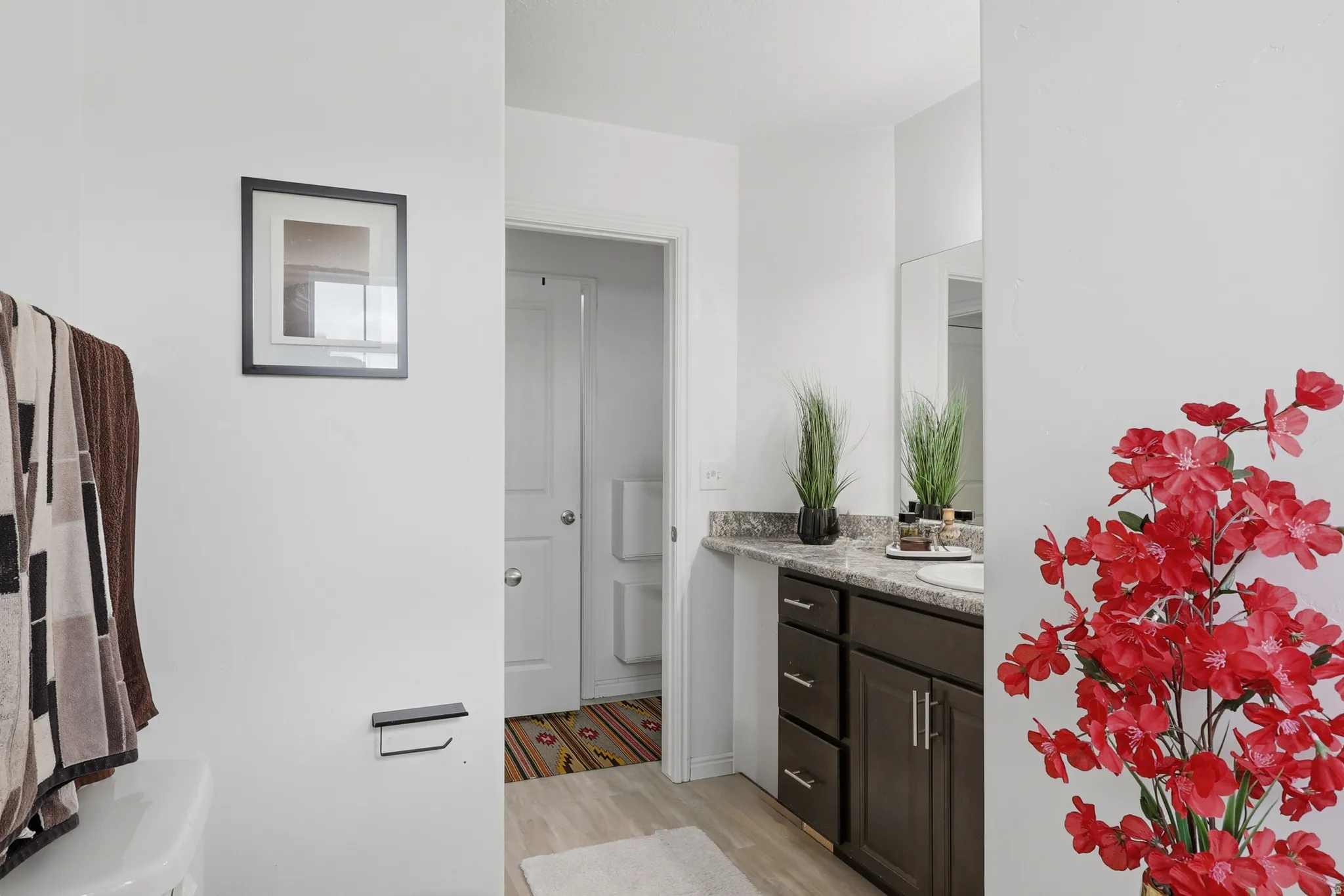 Bathroom vanity featuring dark wood-finish cabinetry, a stone-finish countertop, and an integrated white sink