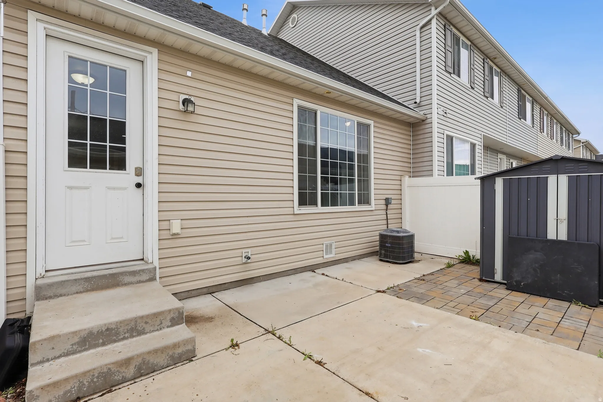 Concrete patio with a storage shed, white vinyl fencing, and an exterior door with grid-patterned glass