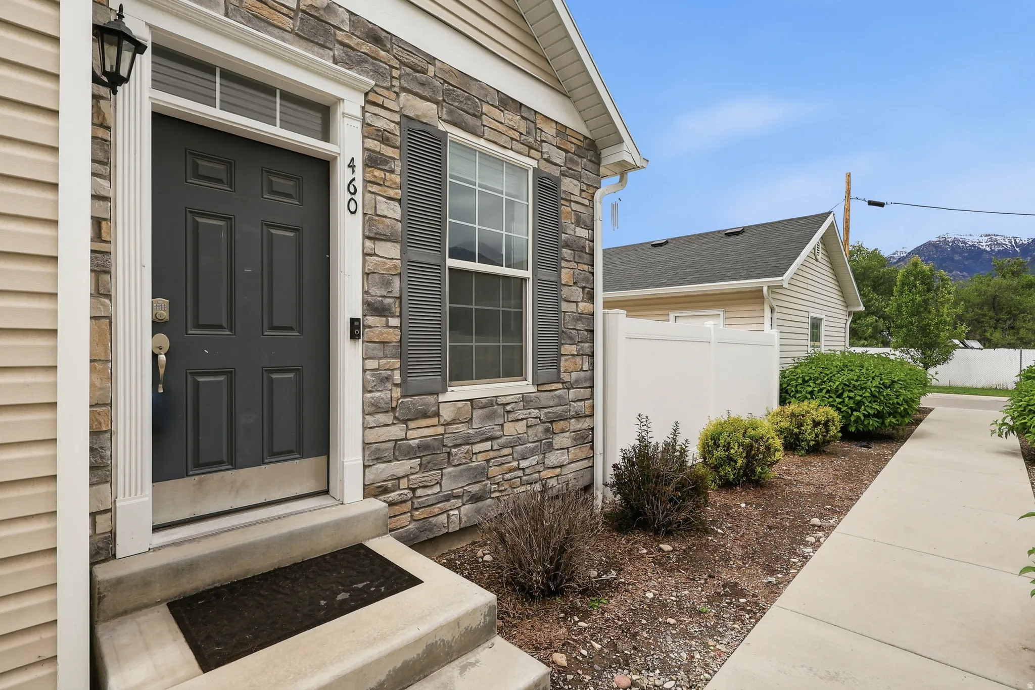 Exterior showcasing stone veneer siding, horizontal vinyl siding, a dark paneled entry door with transom window, decorative window shutters, and a concrete pathway