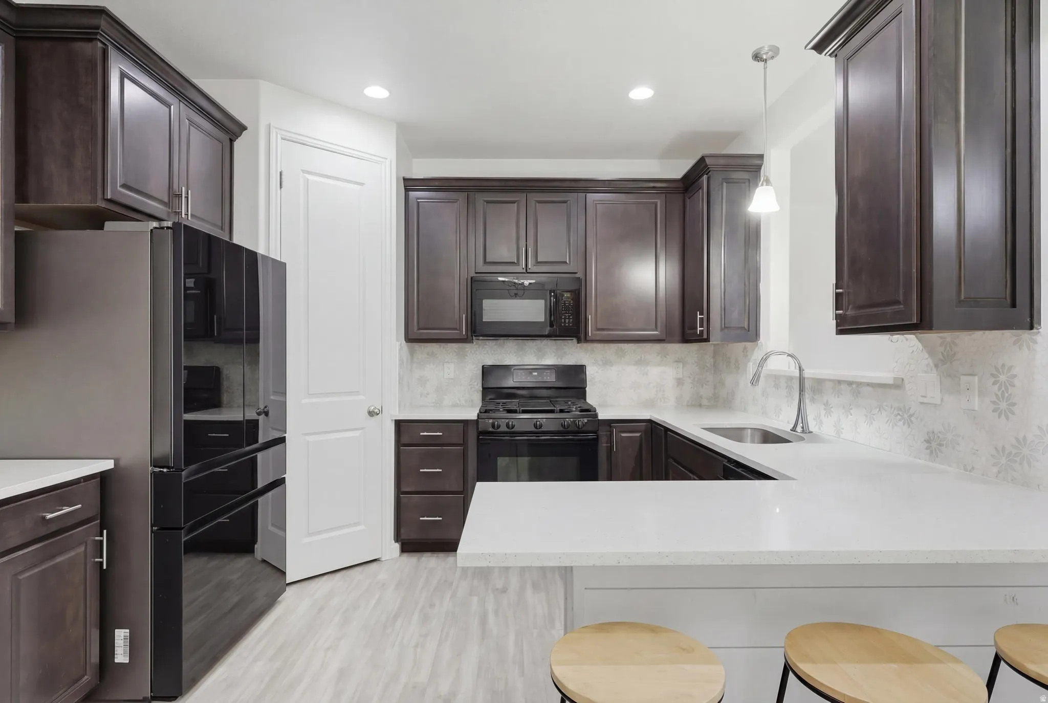 Kitchen featuring espresso cabinetry, light-toned countertops, a patterned backsplash, stainless steel sink, and wood-finish flooring