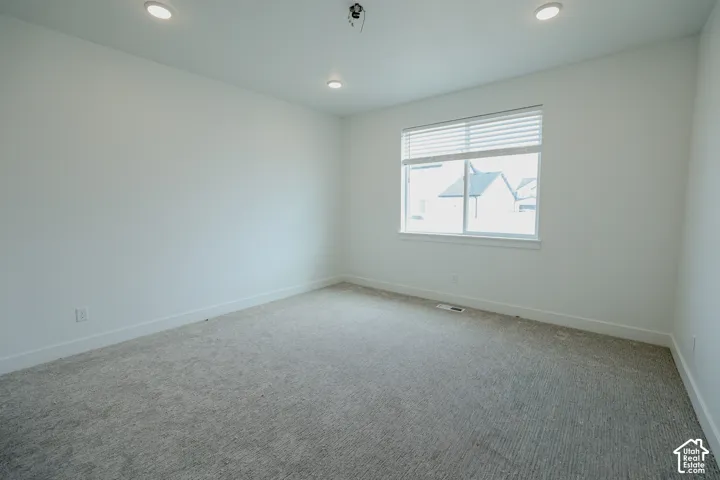 Carpeted room featuring a single window with horizontal blinds, recessed ceiling lighting, and crisp white baseboards