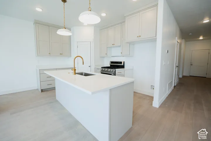 Contemporary kitchen featuring a center island with an undermount sink and brass faucet, light-colored cabinetry with brass hardware, a stainless steel range, and wood-finish flooring