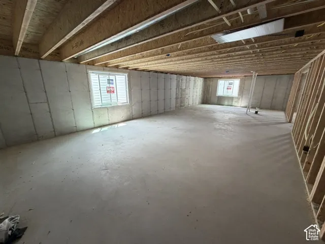 Spacious unfinished basement featuring concrete flooring, exposed wood joists, framed walls, and two visible windows