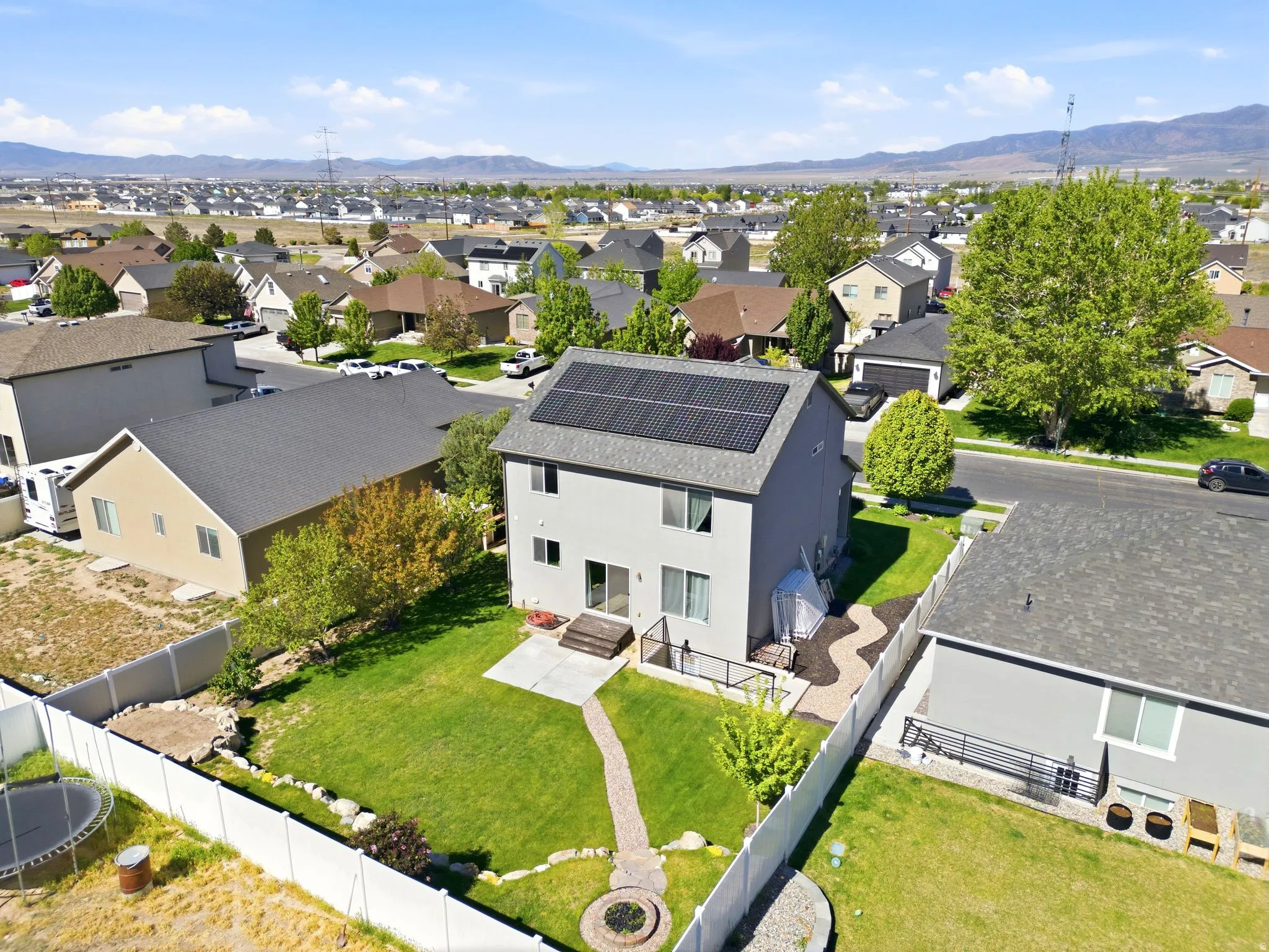 Two-story dwelling featuring a gray exterior, rooftop solar panels, a manicured lawn, and a brick pathway leading to a fire pit