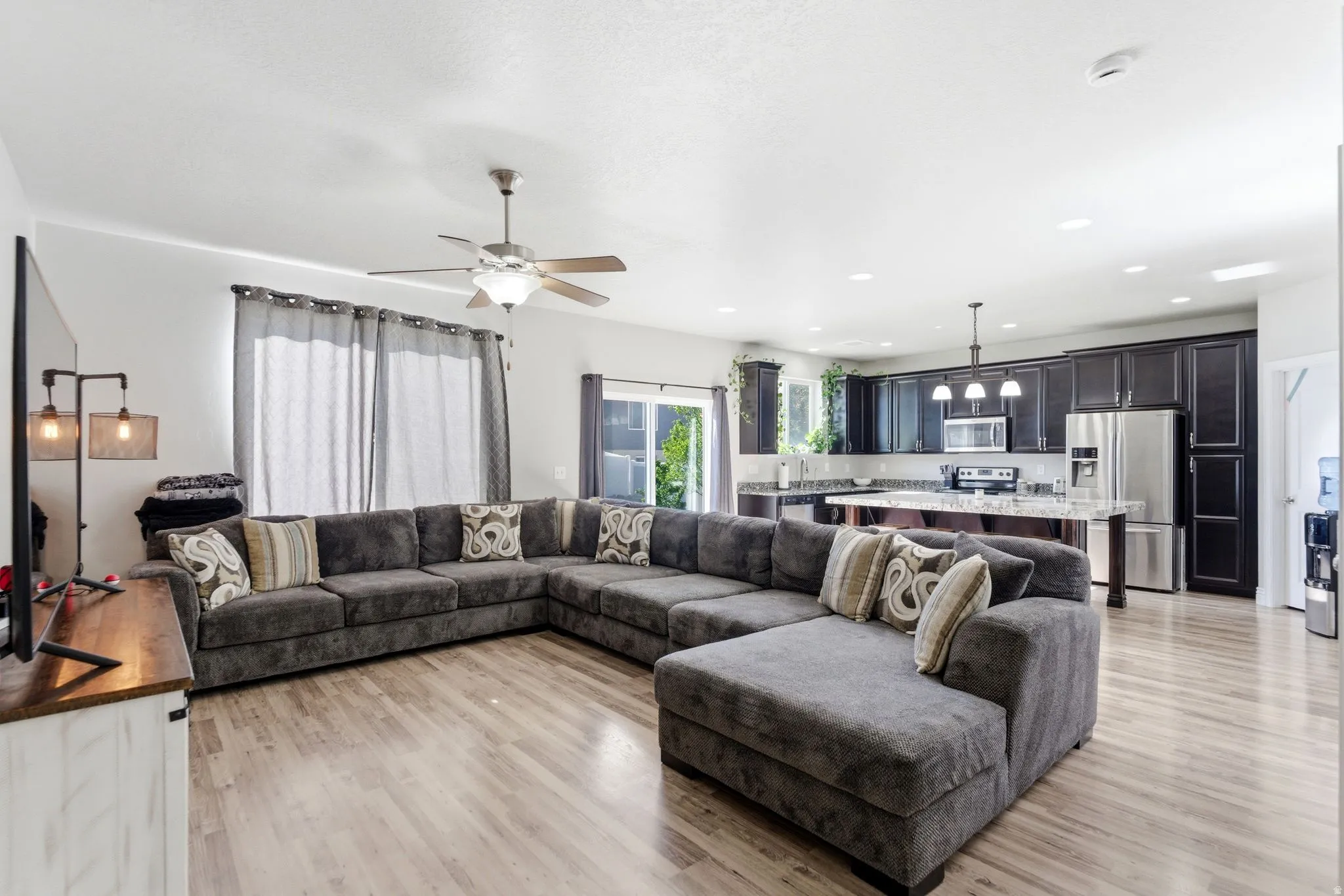 Open-concept living space featuring wood-finish flooring, a ceiling fan with light fixture, and recessed lighting