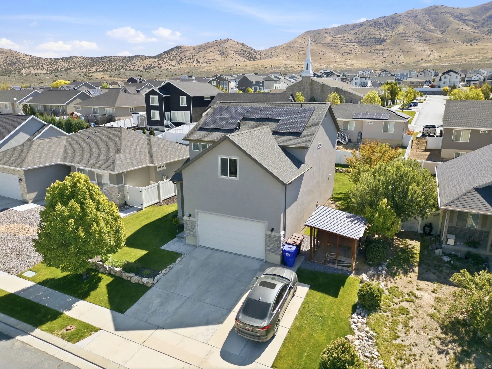 Contemporary residence featuring a two-car garage with a concrete driveway, a gabled roof with solar panels, and a covered patio structure