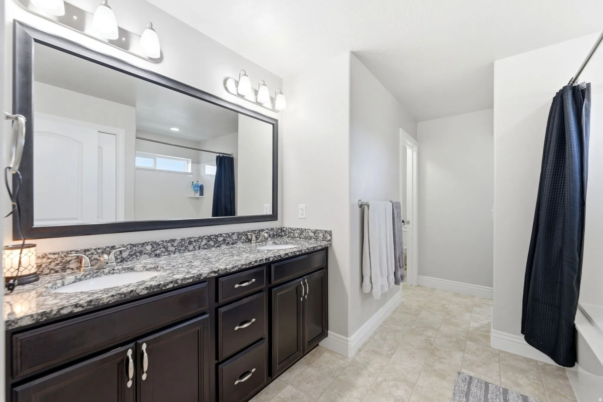 Dual vanity featuring a granite countertop with integrated sinks, dark wood cabinetry, and an expansive framed mirror