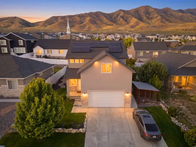 Two-story stucco exterior featuring an attached two-car garage, solar panels, and a stone facade accent