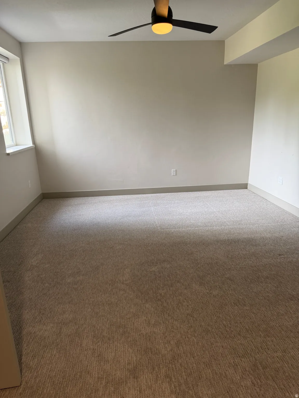Expansive room featuring neutral-toned carpeting, a contemporary ceiling fan, and ample natural light from the window