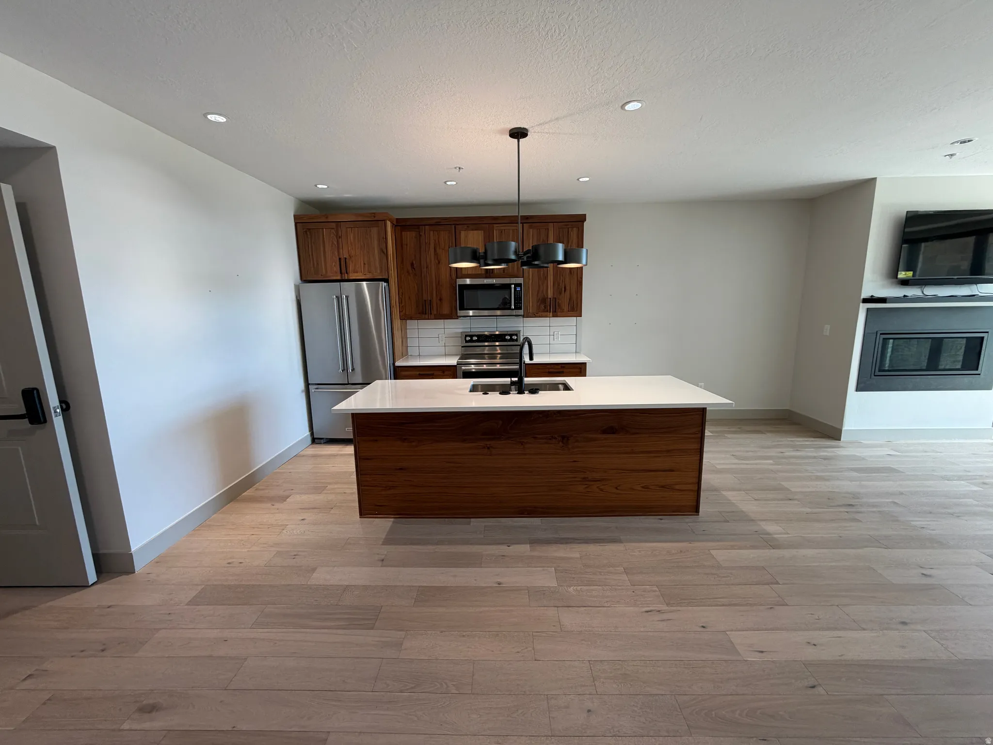 Open-concept kitchen featuring a central island with a white countertop and wood-finish base, stainless steel appliances, a white subway tile backsplash, and recessed lighting