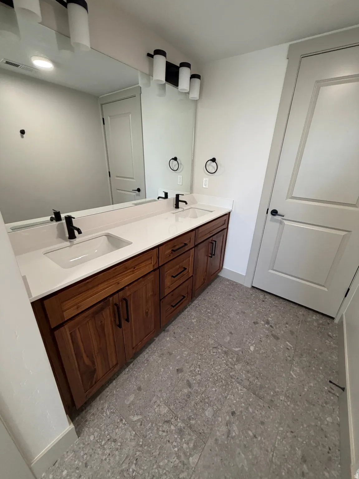 Dual vanity featuring wood-finish cabinetry, white countertops, and matte black fixtures