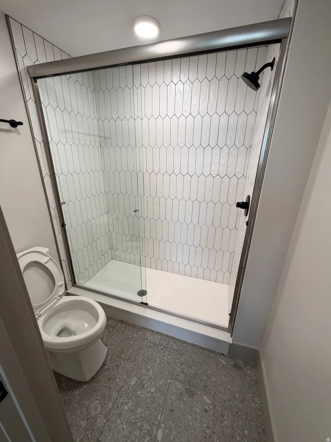 Walk-in shower featuring patterned tile surround, glass enclosure, black shower fixtures, and a white shower pan