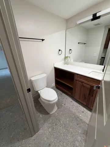 Bathroom featuring a white toilet, wood-finish vanity with open shelving and cabinet storage, white countertop with integrated sink, and large wall-mounted mirror with linear lighting fixture