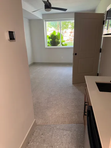 Well-lit room featuring a large window, a ceiling fan, and carpet flooring