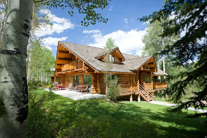 Rustic log cabin exterior with a shingle roof, multiple gables, and a visible second-story balcony