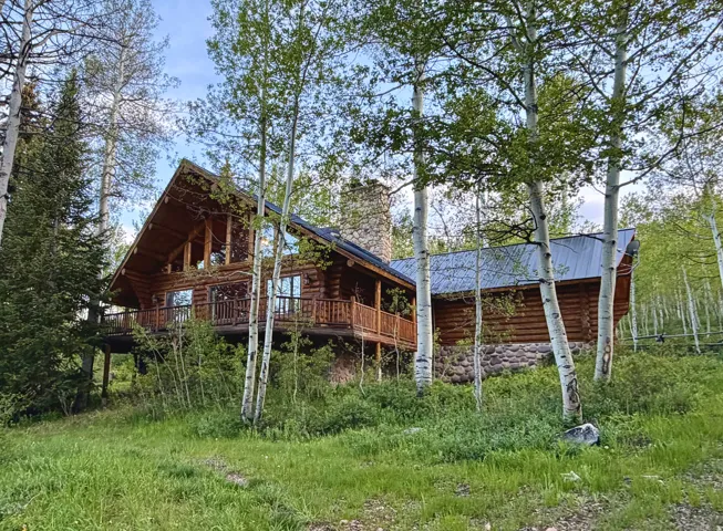 Log cabin residence featuring a prominent stone chimney, a metal roof, and an expansive wrap-around deck