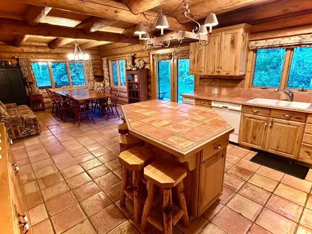 Expansive kitchen and dining area featuring natural wood log walls and ceilings, tile flooring, and a kitchen island with a tiled countertop