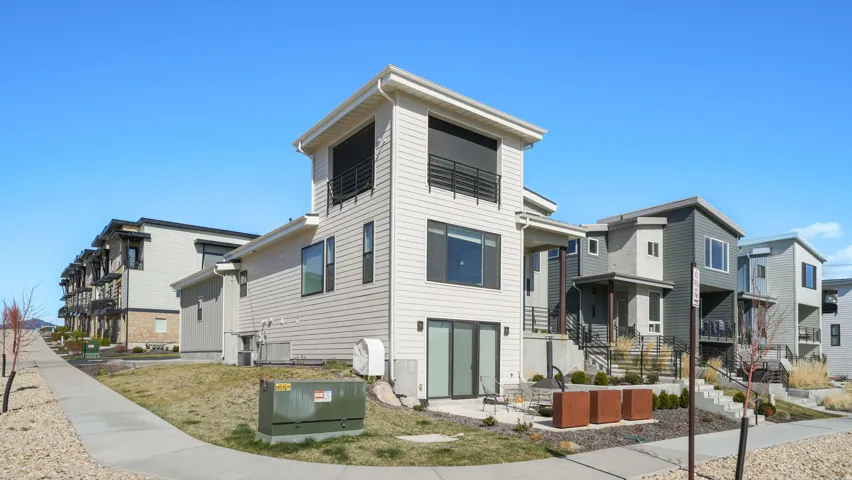 Modern multi-story property featuring light-colored siding, a second-story balcony with dark railings, and a ground-level patio with sliding glass doors