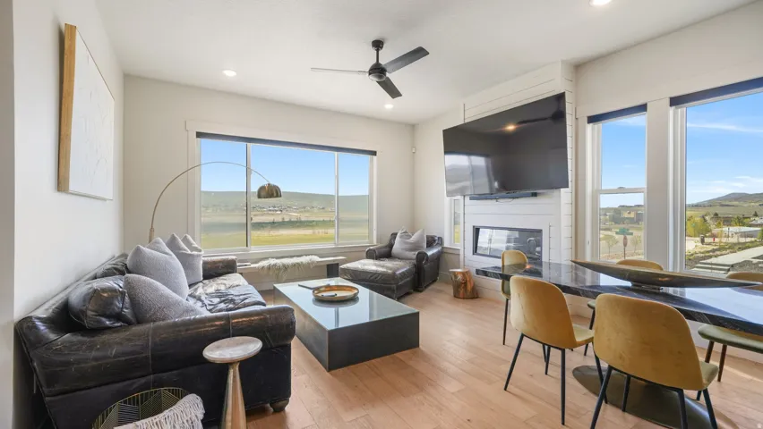 Open-concept living space featuring wood-finish flooring, a contemporary fireplace with a shiplap surround, and abundant natural light from multiple large windows