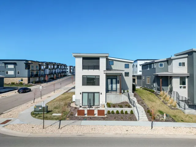 Modern multi-level residence featuring a white and gray exterior, prominent upper-level balcony, ground-floor patio, and a terraced front landscape with a concrete staircase