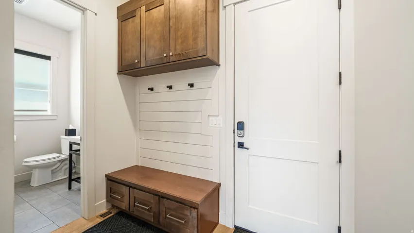 Mudroom entry with built-in bench seating, upper cabinetry, and coat hooks