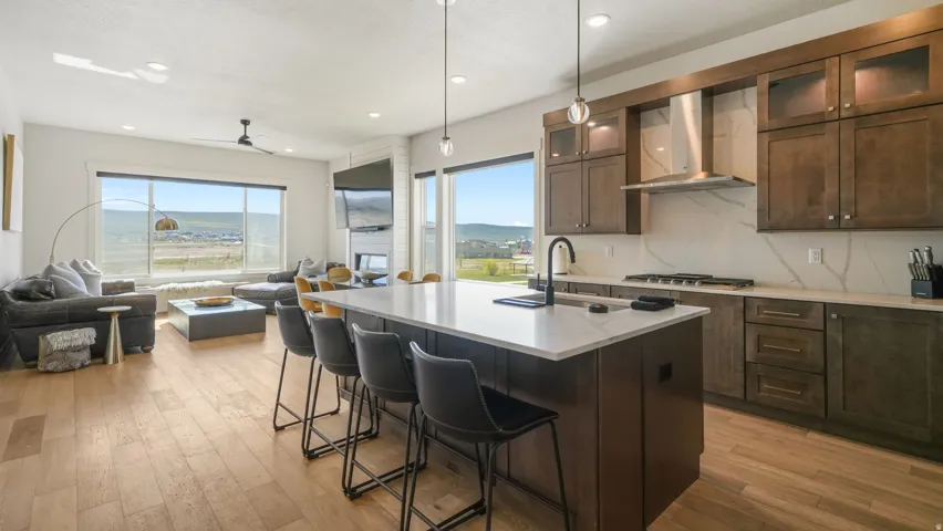 Open concept kitchen and living area featuring a large center island with seating, a built-in gas range, wood-finish flooring, and expansive windows