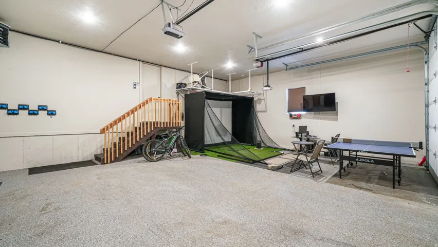 Spacious garage featuring epoxy flooring, overhead lighting, a built-in wooden staircase, and a visible garage door