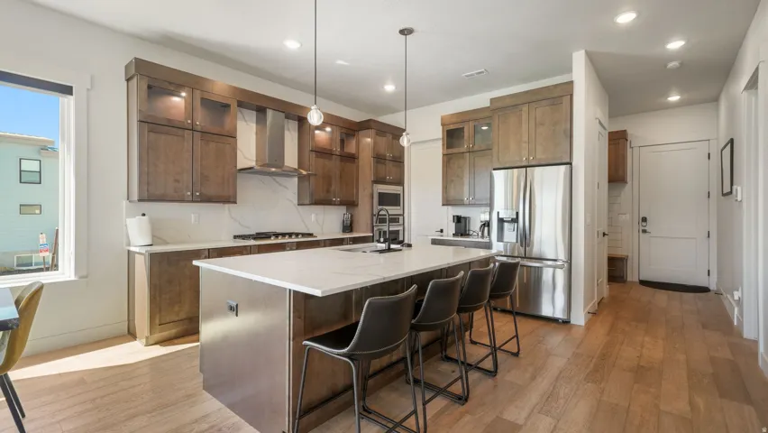 Modern kitchen featuring an expansive center island with quartz countertop and seating, stainless steel appliances, custom wood cabinetry, and wood-finish flooring