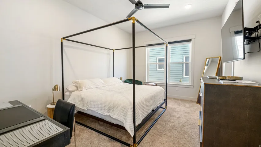 Carpeted bedroom featuring a ceiling fan, dual windows with blinds, a wall-mounted television bracket, and a built-in recessed light fixture