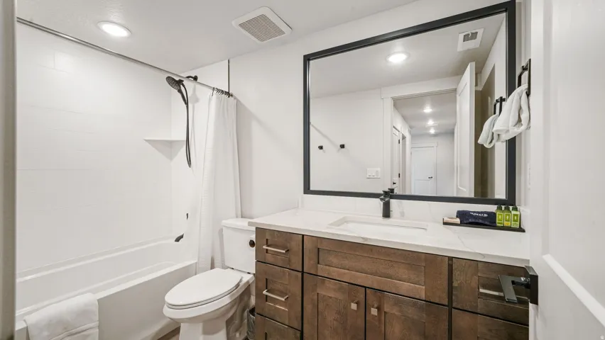 Contemporary bathroom featuring a wood-finish vanity with a white countertop and undermount sink, a large framed mirror, a white subway-tiled shower/tub combination, and matte black fixtures