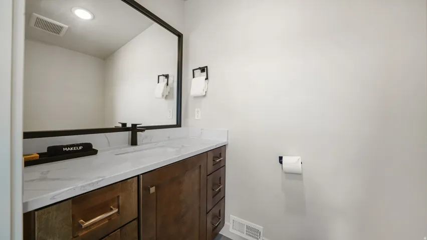 Contemporary bathroom vanity featuring a rectangular undermount sink, a marble-patterned countertop, dark wood-finish cabinetry with varied hardware, and a large framed mirror with a matte black faucet