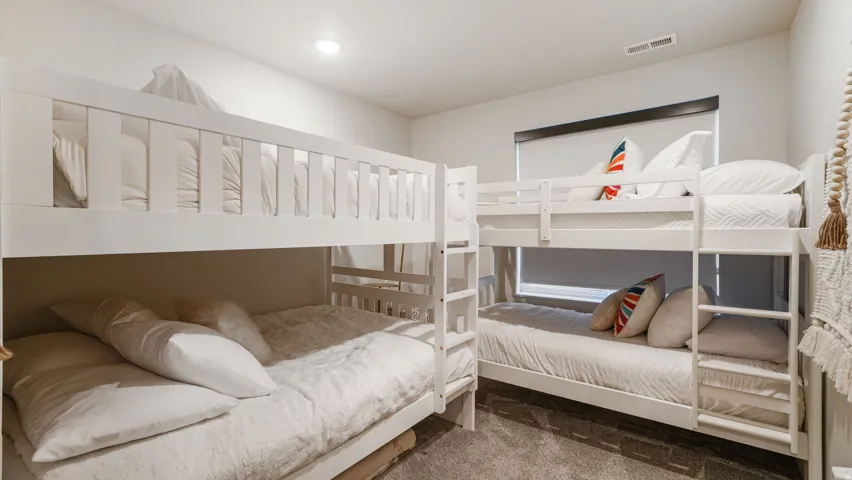 Room featuring two white bunk bed frames, recessed ceiling lighting, and a window with a roller shade