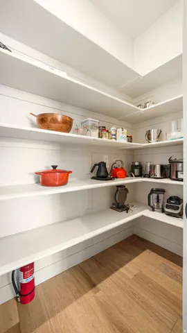 Spacious pantry featuring extensive wrap-around shelving, clean white finishes, and wood-finish flooring