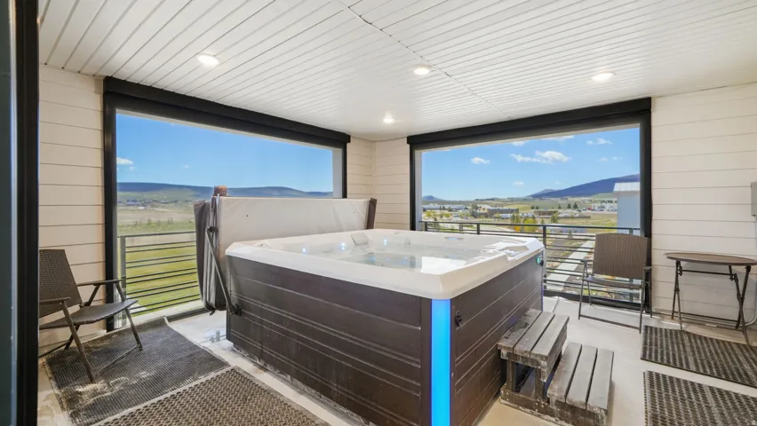 Covered outdoor balcony featuring a built-in hot tub with integrated lighting, wood-plank steps, and panoramic mountain scenery